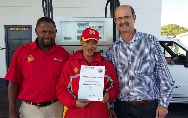 Schalk  Strauss (regs),  bestuurder  van  Birkenhead  Motors,  oorhandig  ‘n kontantprys  en  sertifikaat  aan  Christine Bester.   Claude  Vanqa,    area-bestuurder van Shell staan by.