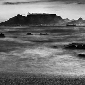 Nog ‘n besonderse foto deur Robert Johnson, Gansbaai Fotografieklub se opleidingsfotograaf, met ‘n wasige (blurred) oseaan op die voorgrond en ‘n duidelike beeld van Tafelberg en ‘n boot op die agtergrond. 