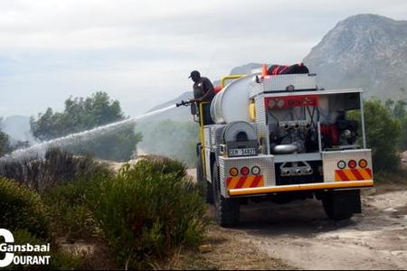 Enkele veldbrande rondom Gansbaai en in die omgewing het weer die afgelope tyd ontstaan.  Hier is Gallie Badenhorst agter die stuur besig terwyl brandweerman Thembelani Xovula probeer om die smeulende veldbrand onder beheer te bring.