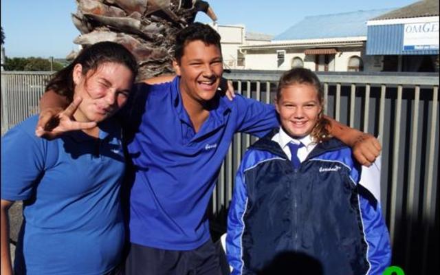 Van die getroue ‘hekwagte’ wat die skoolhek beman en programme verkoop  tydens groot sportdae by Laerskool Gansbaai, word maklik oorgesien, maar sonder hulle vriendelike hulp kan ‘n sportdag nie aangebied word nie. Dankie vir julle bydrae tot sportdae. Van links glimlag  Leandra Theart, Henrique Lourens en Rianka Slabber – al drie is 12 jaar oud en in graad 6.