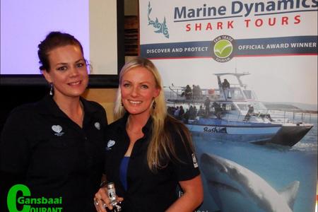 Alison Towner (right), white shark biologist for the Dyer Island Conservation Trust,  receives a bottle of wine after enlightening guests at the recent Marine Evening in the Great White House. With her is Cari du Preez, Marketing Manager.