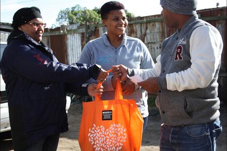 Pinkey Ngewu (DICT) together with Belnay van Tonder (Great White House) handing over a food parcel gift to 1st year DEEP student Vanashree Lottering’s dad.