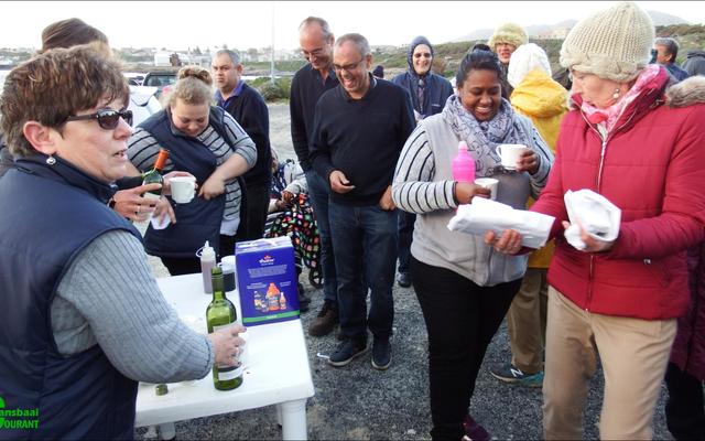 Soos natgereënde hoenders tydens Gansbaai Toerisme se “Sunset Walk”. Links by die tafel bedien Glenda Kitley en Doulene Els van Gansbaai Toerisme die deelnemers, met Maureen Valentine wat na Sharman Geldenhuys, bibliotekaresse, omsien.