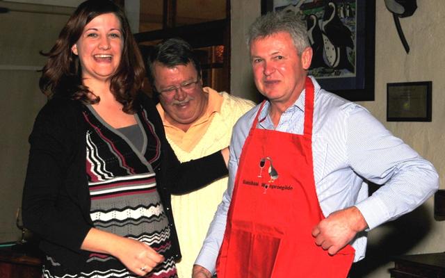 ‘n Gesellige wynproe-aand word tradisioneel met ‘n Gansbaai Wynproegilde geskenkvoorskoot afgesluit. Regs spog die wynmaker van Durbanville Hills Wyne, Kobus Gerber, met sy rooi voorskoot. Nelleke Ferreira staan links by die voorsitter, Theuns Roodman wat die voorskoot oorhandig het. (Foto: Jane Bailey) 